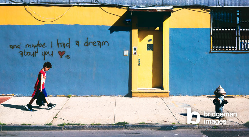 photography of a child walking in front of a blue wall with graffiti in the back