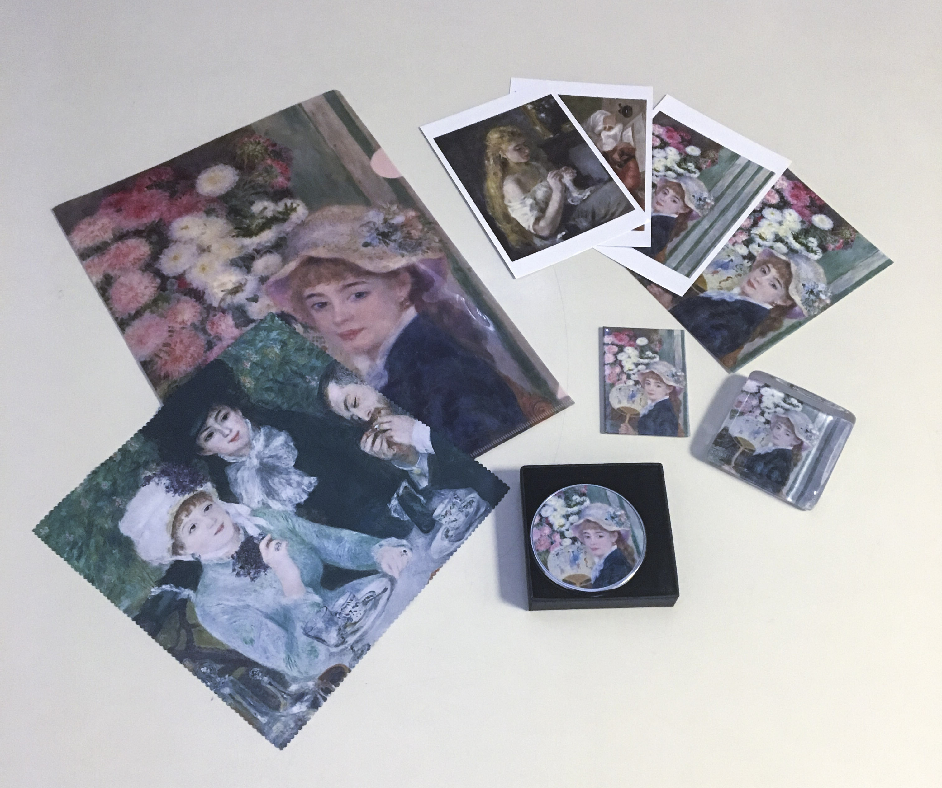 Image of the range of exhibition materials such as the catalog, postcards, magnets, paper holders, glasses cloth, compact mirrors and paper folders featuring Renoir images